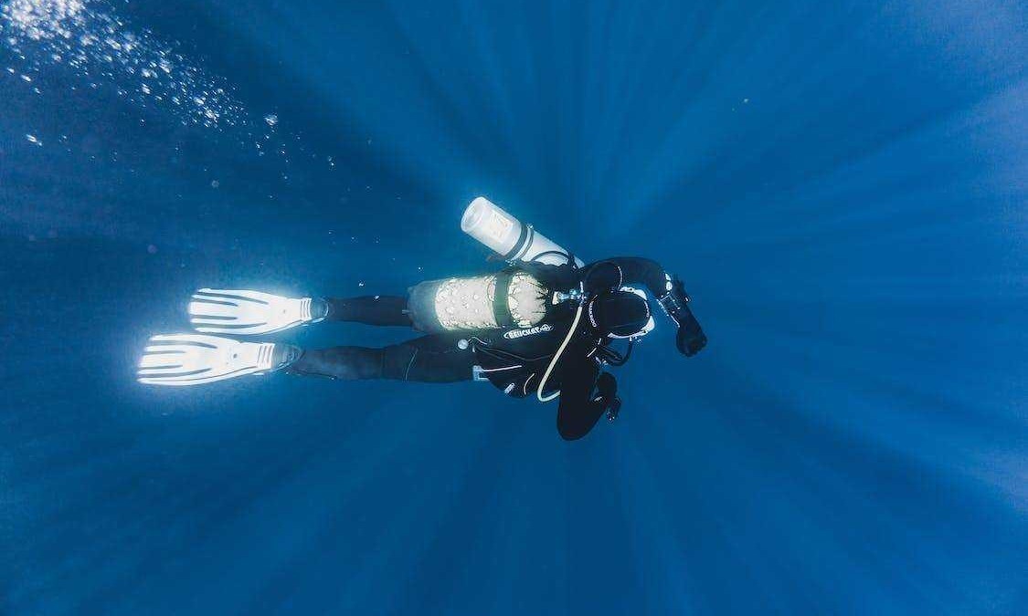 Immersione subacquea in acqua blu con attrezzatura da diving, snorkel, muta e bombole, esplorando il mondo marino e la fauna sottomarina. Attività di avventura e turismo subacqueo.