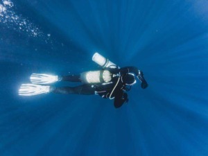 Immersione subacquea in acqua blu con attrezzatura da diving, snorkel, muta e bombole, esplorando il mondo marino e la fauna sottomarina. Attività di avventura e turismo subacqueo.