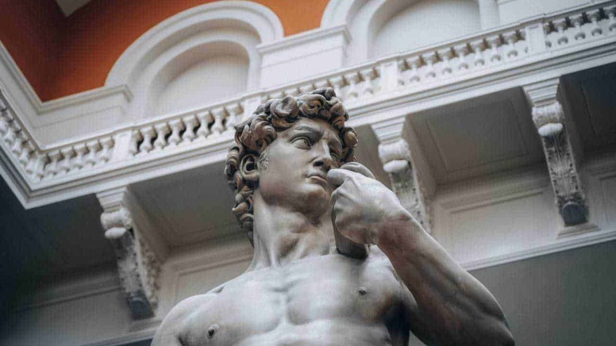 Statua di David di Michelangelo, replica in marmo all'interno di un museo con dettagli architettonici classici, simbolo di arte rinascimentale e perfezione artistica in Italia.