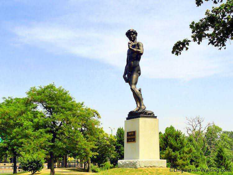 Statua di bronzo raffigurante il David di Michelangelo in un parco verdeggiante, simbolo di arte e cultura italiana all'aperto.