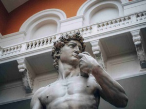Statua di David di Michelangelo, replica in marmo all'interno di un museo con dettagli architettonici classici, simbolo di arte rinascimentale e perfezione artistica in Italia.