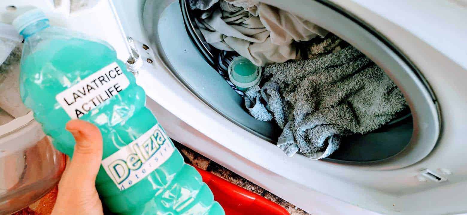 Lavatrice con detersivo in polvere, macchina da bucato con vestiti bianchi e colorati, lavaggio dei capi.