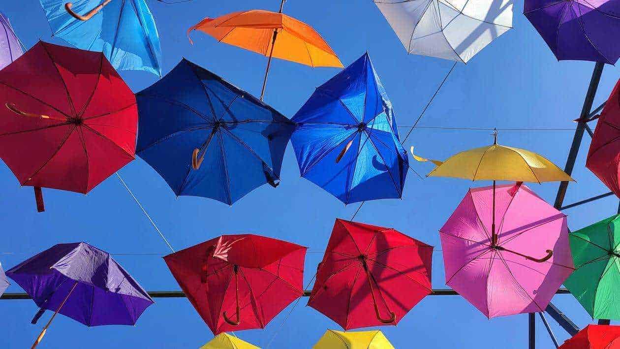 Colorati ombrelli appesi contro un cielo azzurro, creano un'installazione artistica estiva all'aperto. Un'idea originale per decorazioni di strada e ambienti urbani, ideale per foto creative e Instagram.