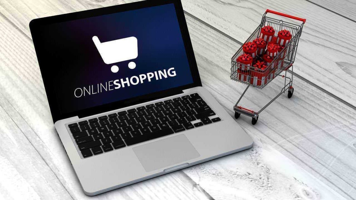 Carrello della spesa con regali natalizi su una scrivania, simbolo di shopping online durante le festività.