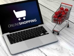 Carrello della spesa con regali natalizi su una scrivania, simbolo di shopping online durante le festività.