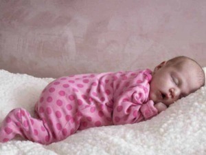 Neonato che dorme su coperta morbida, vestito rosa con pois, riposo sereno, aspetto tranquillo, immagine dolce di un bebè, cura neonatale, infanzia felice, tenerezza.