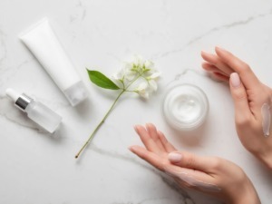 Crema idratante e prodotti skincare naturali con fiori freschi su superficie marmo bianco. Ritratto di routine di bellezza e cura della pelle con ingredienti di origine naturale.