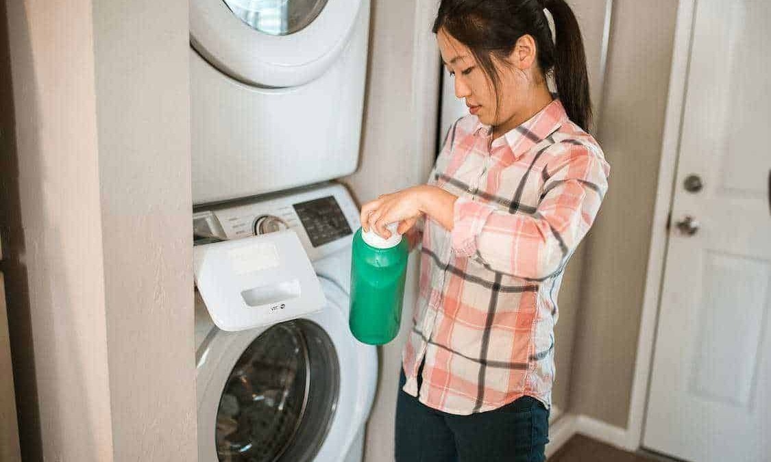 Lavatrice e detersivo in uso, donna che riempie la lavatrice con detersivo liquido, pulizia e cura del bucato, contesto domestico, servizio di lavanderia.