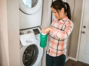 Lavatrice e detersivo in uso, donna che riempie la lavatrice con detersivo liquido, pulizia e cura del bucato, contesto domestico, servizio di lavanderia.