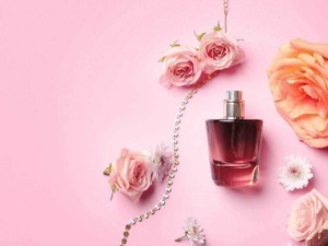 Profumo femminile con fiori rosa e collana decorativa su sfondo rosa pastello.