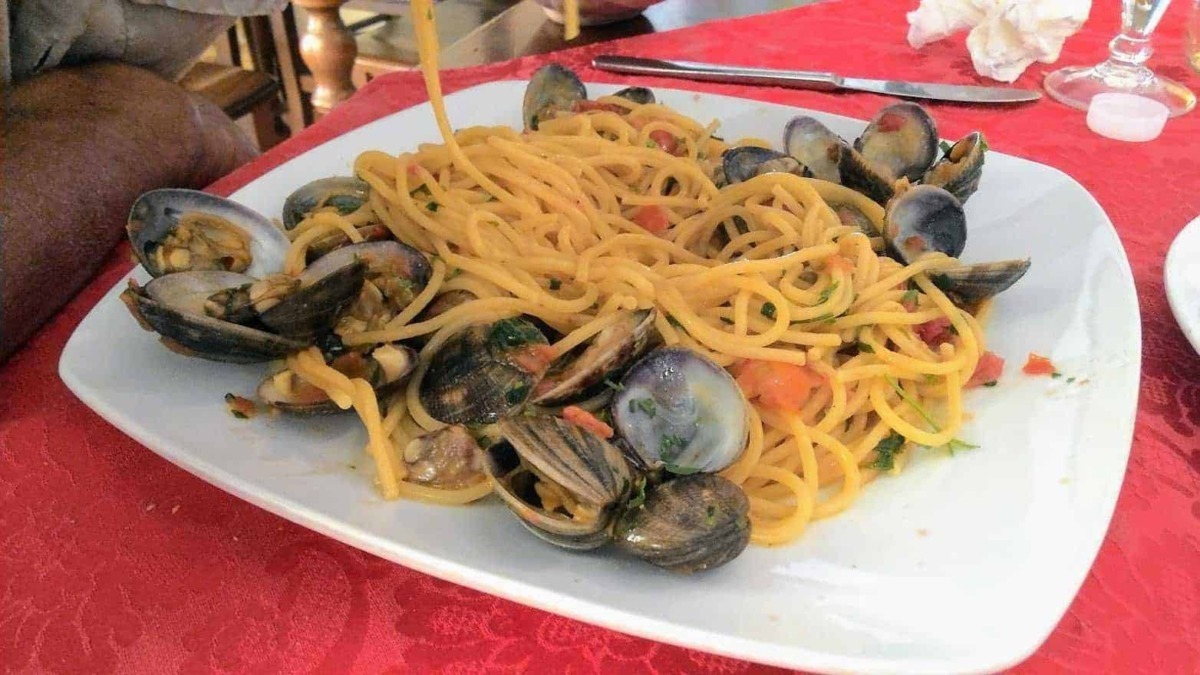 Spaghetti alle vongole su piatto bianco con tavolo rossa, pasta italiana con molluschi freschi, piatto di mare tipico della cucina tradizionale italiana, gustoso e appetitoso.