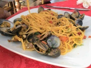 Spaghetti alle vongole su piatto bianco con tavolo rossa, pasta italiana con molluschi freschi, piatto di mare tipico della cucina tradizionale italiana, gustoso e appetitoso.