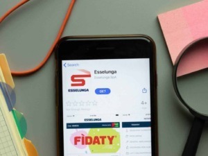 Appunti Sul Blog, immagine di uno smartphone con app Esselunga nel display, circondato da oggetti colorati e di design in un ambiente di lavoro o studio.