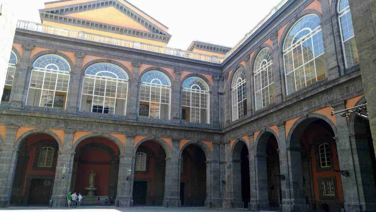 Grande edificio storico con arcate e grandi vetrate, stile architettonico classico, situato in una piazza pubblica, suggestiva illuminazione naturale, facciata ornata di dettagli eleganti, rappresenta patrimonio culturale e architettonico.