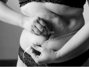 Misurazione della vita quotidiana, ritratto in bianco e nero di una donna che utilizza un metro per controllare il proprio addome, simbolo di autocura e benessere fisico.