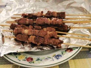 Spiedini di carne alla griglia su piatto decorato, pronti per essere gustati, con bullone di carta argentata e tavola a scacchi in tessuto casual.
