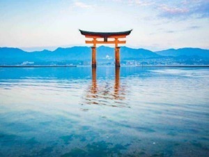 Torii tradizionale giapponese immerso nel mare con montagne sullo sfondo, simbolo di spiritualità e cultura nipponica, perfetto per articoli su viaggi, cultura e religione in Giappone.