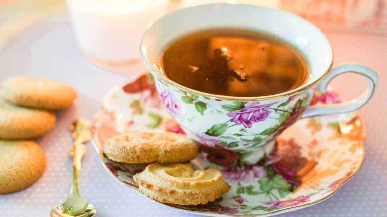 Cucina inglese, i 5 piatti che devi mangiare se vai a Londra 4 Tazza di tè in una tazza di porcellana decorata con motivi floreali, accompagnata da biscotti tradizionali su un piattino abbinato, ideale per un momento di relax e dolcezza.