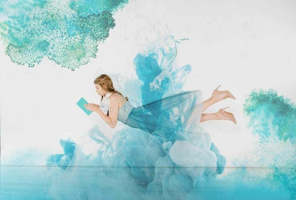 Ragazza che legge un tablet, immersa in un'opera d'arte digitale con sfumature di blu e verde, simbolo di creatività e tecnologia.