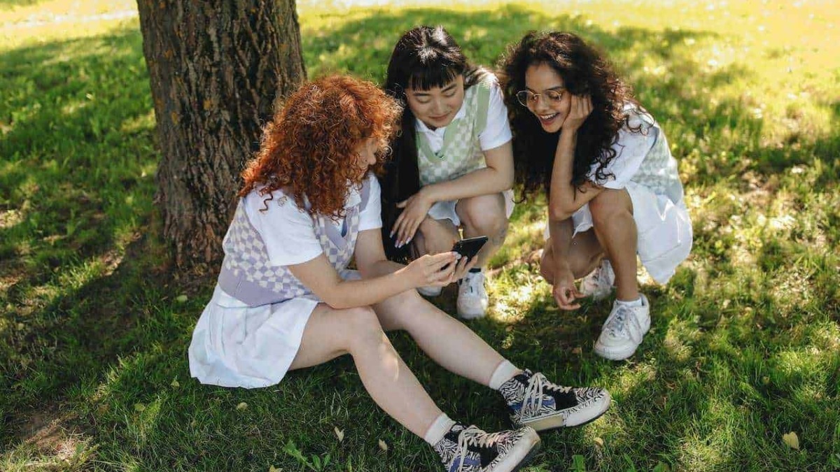 Amiche che cercano ispirazione e condividono contenuti sul blog durante una giornata all'aperto sotto un albero verde.