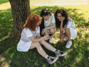 Amiche che cercano ispirazione e condividono contenuti sul blog durante una giornata all'aperto sotto un albero verde.