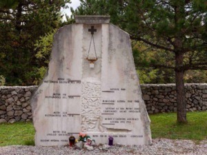 Memoriale di guerra con iscrizioni e fiori all'aperto, dedicato ai caduti durante conflitti tra 1939 e 1945, situato in un'area verde con alberi e muro di pietra.