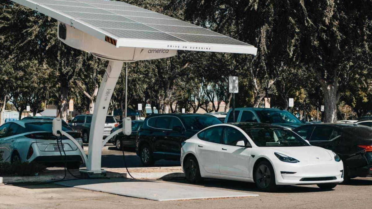 Pannello solare su colonnina di ricarica per veicoli elettrici in parcheggio con auto elettriche, promuovendo energie rinnovabili e mobilità sostenibile.