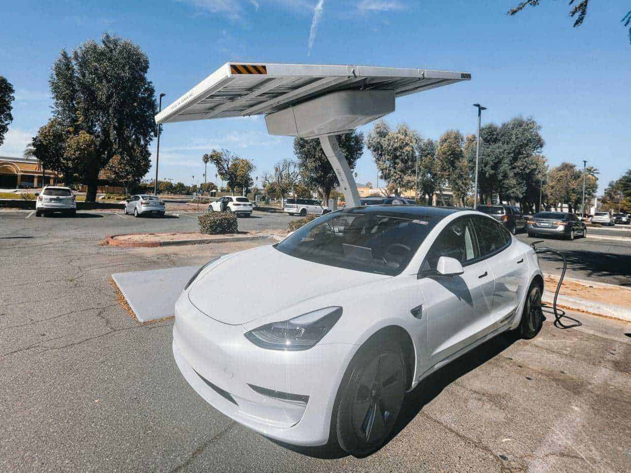Pannello solare su colonnina di ricarica per veicoli elettrici in parcheggio con auto elettriche, promuovendo energie rinnovabili e mobilità sostenibile.