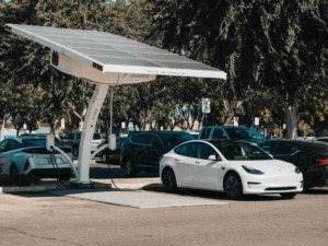 Pannello solare su colonnina di ricarica per veicoli elettrici in parcheggio con auto elettriche, promuovendo energie rinnovabili e mobilità sostenibile.