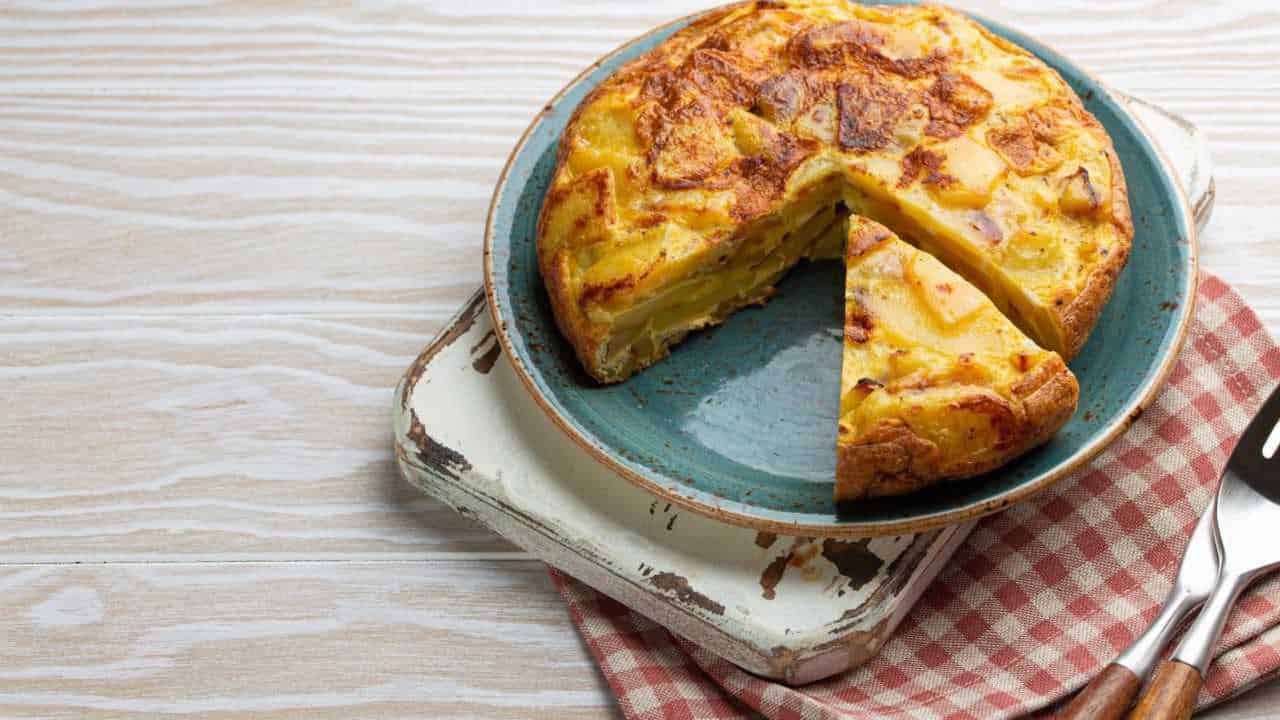 Frittata di patate e formaggio cotta in teglia, pronto da servire, visibile su un piatto azzurro su superficie in legno chiaro, perfetta per ricette di cucina italiana.
