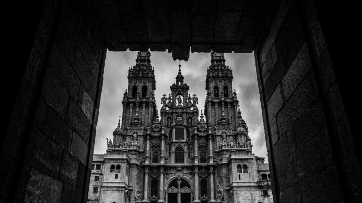 Maestosa chiesa barocca vista attraverso un'apertura in pietra, con dettagli architettonici elaborati e torri che si stagliano contro un cielo nuvoloso.