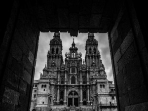 Maestosa chiesa barocca vista attraverso un'apertura in pietra, con dettagli architettonici elaborati e torri che si stagliano contro un cielo nuvoloso.