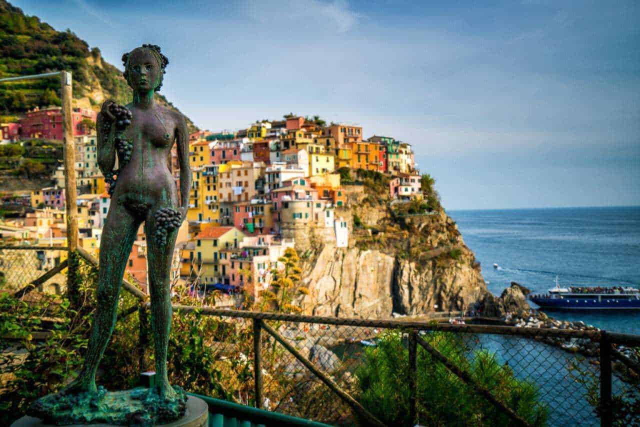 Femminile statua in bronzo sul promontorio di Manarola con visione del borgo colorato delle Cinque Terre e il Mar Ligure sullo sfondo, Italia.