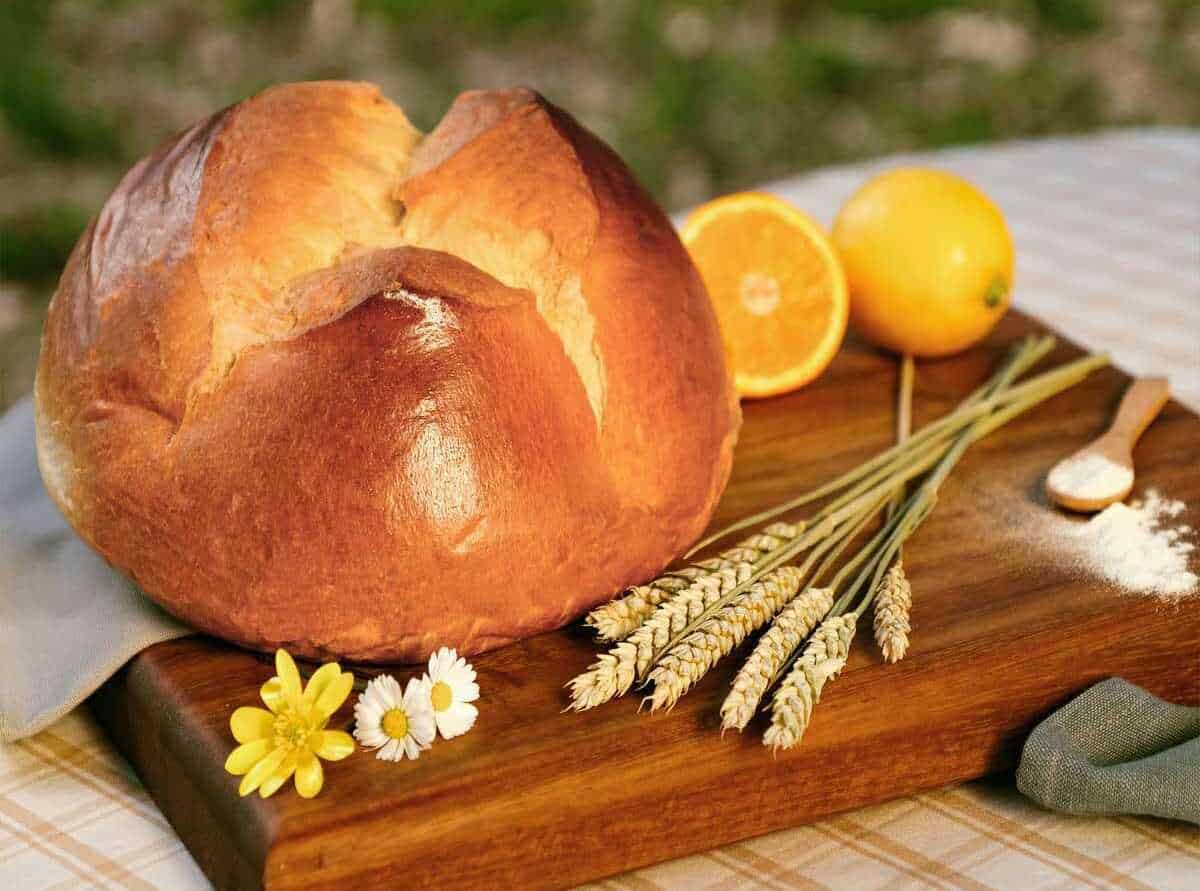 Pane casereccio rustico con scorza dorata, accompagnato da arancia fresca e spiga di grano su tagliere di legno, ideale per ricette tradizionali italiane.