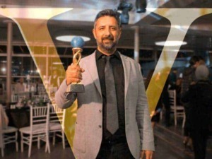 Vincitore con premio Oscar in un evento elegante, uomo sorridente in giacca grigia e cravatta.