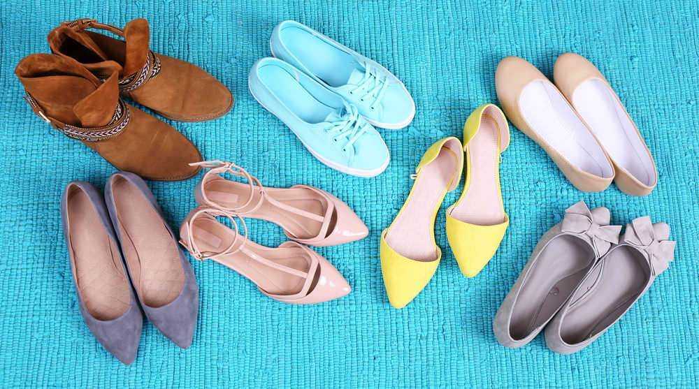 Sandali e scarpe in vari colori e stili disposte su un tappeto azzurro con texture. Scarpe cerimoniali, sportive e casual, ideali per diverse occasioni di moda e stile di vita.