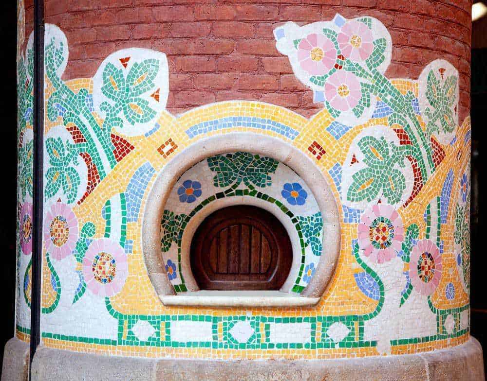 Vaschetta in mosaico colorato con decorazioni floreali e motivi artistici su muro di mattoni rossi.