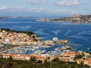 Vita marina e paesaggio costiero con porticciolo, imbarcazioni e case colorate, sotto cielo nuvoloso nella splendida isola mediterranea.