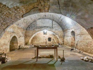 Antica cantina sotterranea con archi in mattoni, utilizzo storico per conservare vino e alimenti, ambiente suggestivo e ricco di storia.