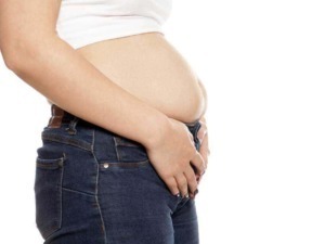 Gonfiore addominale e gravidanza: immagine di una donna con pancia prominente, indossando jeans e maglietta bianca, simbolo di dolori e cambiamenti durante la gravidanza.