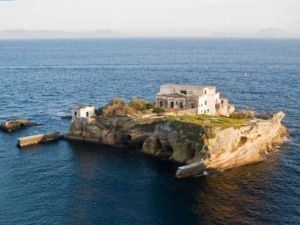 Antico fortino sulla scogliera in mare, murazzi e costruzioni storiche, isola diroccata circondata da acque blu profonde, paesaggio marino mediterraneo.