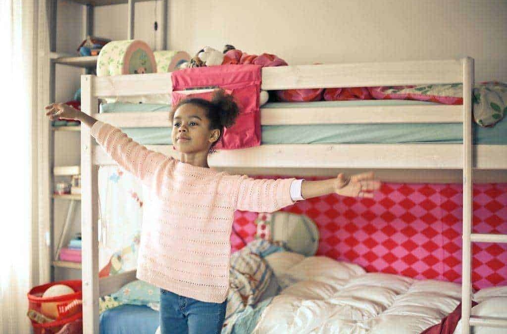 Lettera l'immagine di una bambina che si allarga con le braccia in una camera da letto colorata e accogliente, con un letto a castello e decorazioni giocose.