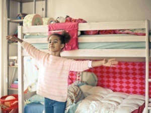 Lettera l'immagine di una bambina che si allarga con le braccia in una camera da letto colorata e accogliente, con un letto a castello e decorazioni giocose.
