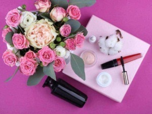 Fiori rosa e bianca con cosmetici e prodotti di bellezza su una tovaglia rosa chiaro, ideale per blog di bellezza, cura della pelle e routine di trucco. Composizione elegante e femminile.