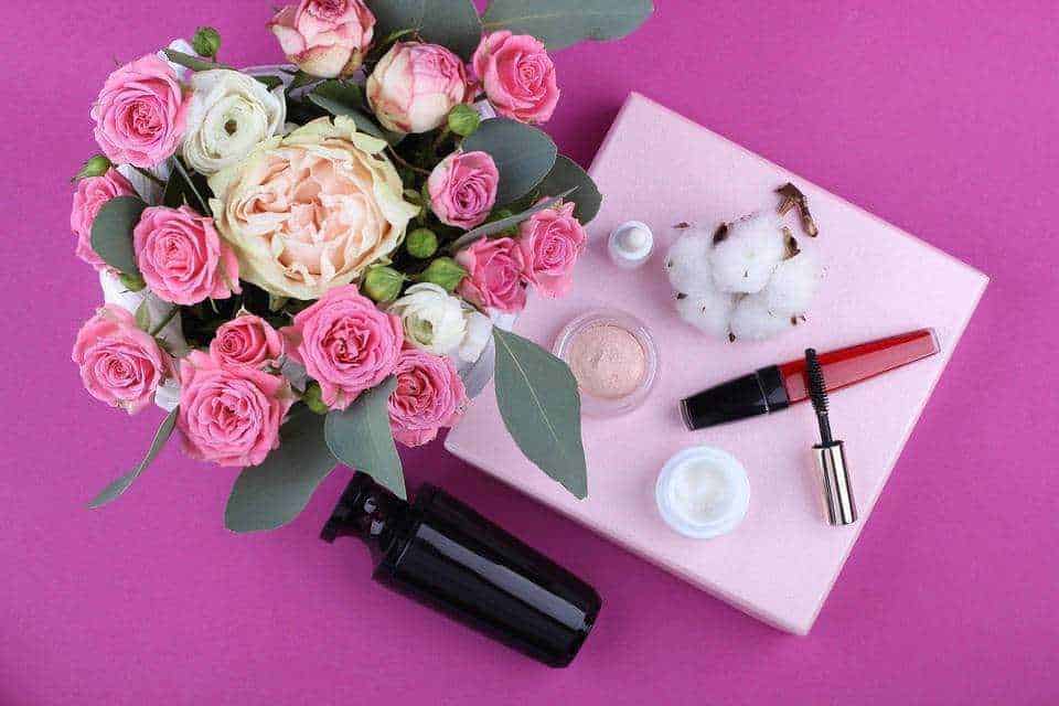Fiori rosa e bianca con cosmetici e prodotti di bellezza su una tovaglia rosa chiaro, ideale per blog di bellezza, cura della pelle e routine di trucco. Composizione elegante e femminile.