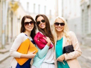 Vivian o ragazze alla moda con occhiali da sole sorridenti passeggiando in città, indossando abbigliamento trendy e accessori colorati, in un contesto urbano di giorno.