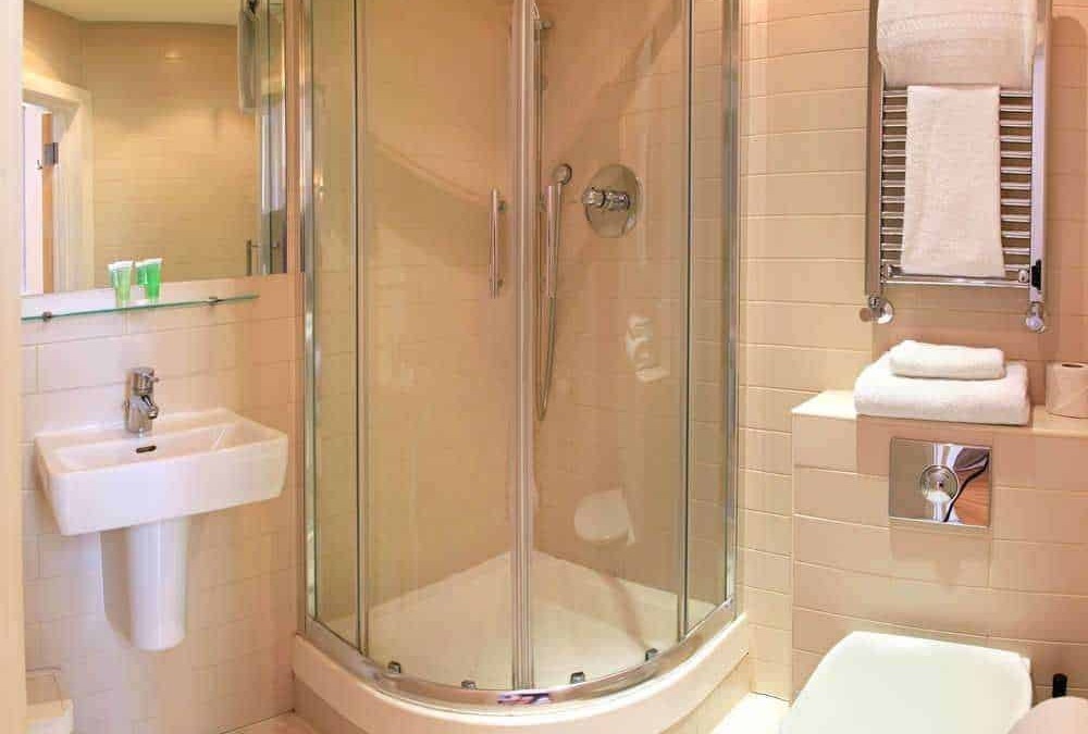 Doccia moderna in bagno di hotel, sanitari bianchi, asciugamani piegati su radiatore in acciaio, ambiente pulito e luminoso, ideale per soggiorni comfort e relax.