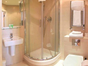Doccia moderna in bagno di hotel, sanitari bianchi, asciugamani piegati su radiatore in acciaio, ambiente pulito e luminoso, ideale per soggiorni comfort e relax.