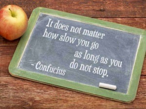 Scritte motivazionali su lavagna con mela su tavola di legno, citazione di Confucio sull'importanza della persistenza e della costanza. Immagine perfetta per ispirare impegno e determinazione.