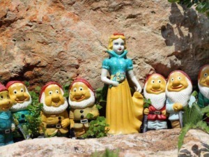 Colorati gnomi da giardino con statua di Biancaneve, decorazioni da esterno, ambientazione naturale con pietre e piante, ideale per giardini e spazi all'aperto, decorazioni fantasiose.